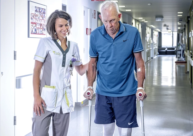 Verpleegkundige en patiënt met krukken door de ziekenhuisgang